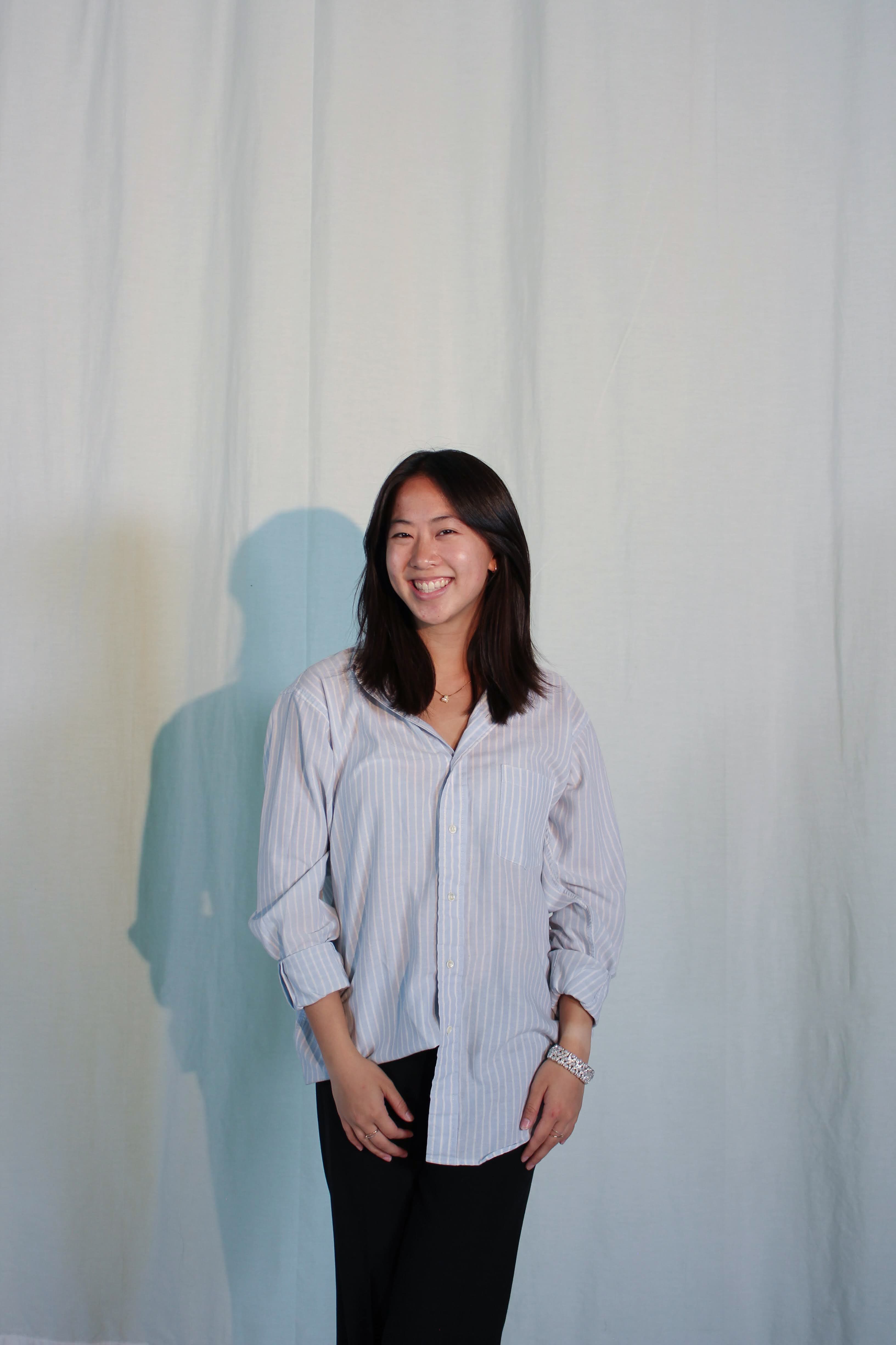 Shannon Chen smiling in a striped shirt against a pale curtain